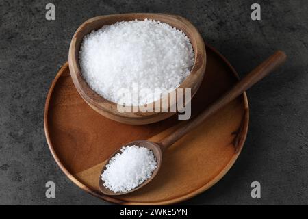 Natürliches Salz in Holzschale und Löffel auf dunkelgrauem Tisch Stockfoto