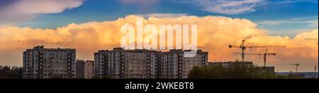 Wunderschönes Panorama der Stadtlandschaft gegen Sonnenuntergang am bewölkten Himmel. Wohngebäude und Baukräne. Stockfoto