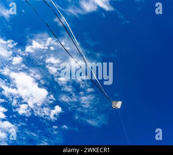 Ein Drachen, der in de panne vor einem blauen Himmel mit ein paar kleinen Wolken fliegt Stockfoto