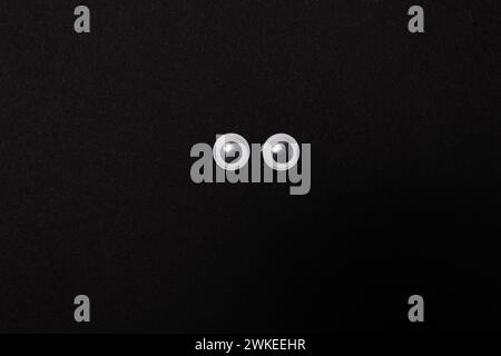 Nahaufnahme von Googly Eyes auf schwarzem Hintergrund mit Kopierraum Stockfoto