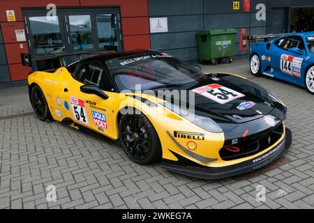 Dreiviertel-Vorderansicht eines Ferrari 458 Challenge in Schwarz und Gelb, die für das Rennen vorbereitet wurde, im internationalen Paddock in Silverstone Stockfoto