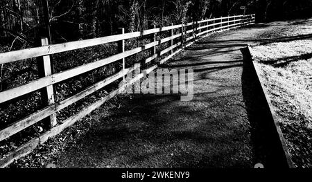 Ein Zaun neben einem gemeinsamen Fußweg/Radweg, sonnig vom niedrigen Sonnenwinkel im Winter. Stockfoto