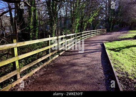 Ein Zaun neben einem gemeinsamen Fußweg/Radweg, sonnig vom niedrigen Sonnenwinkel im Winter. Stockfoto