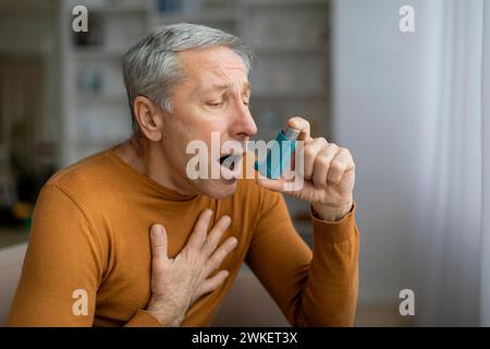 Kranker grauhaariger Senior-Mann, der die Brust berührt und Asthma-Inhalator benutzt Stockfoto