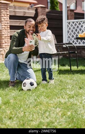 Glücklicher afroamerikanischer Vater und Sohn, der während eines Videoanrufs auf dem Hinterhof auf das Smartphone schaut Stockfoto