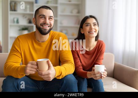 Glückliches Junges Paar Trinkt Kaffee Und Entspannt Auf Der Couch Im Wohnzimmer Stockfoto