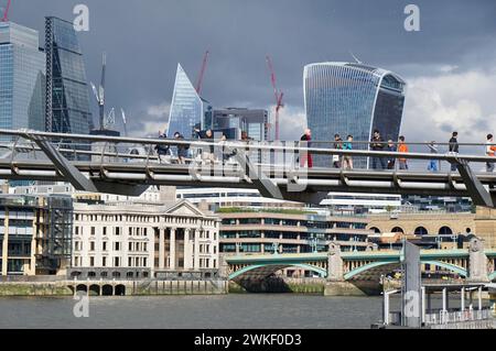 Die Millennium Bridge führt an einem sonnigen Tag durch die moderne Londoner Skyline mit einer dramatischen Kulisse aus stürmischem Himmel. Stockfoto