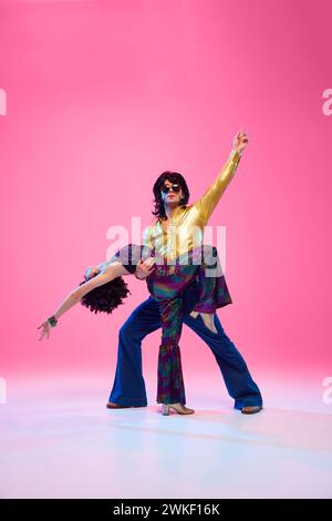 Discoduo Mid-Dance, Mann im Glockenboden, der Partner gegen rosa Studiohintergrund hebt. Künstler in Bewegung. Stockfoto
