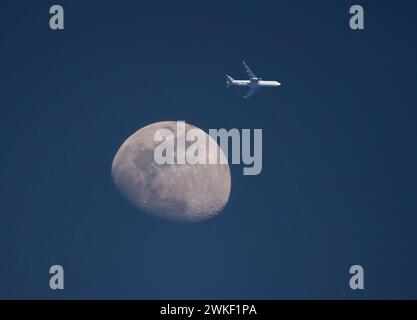 Ein kommerzielles Flugzeug kommt bei Sonnenuntergang in geringer Höhe am Mond vorbei. Stockfoto