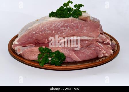 Auf dem Bild liegen ein Stück Schweinefleisch und Zweige eines duftenden Hahns auf einer Tonplatte. Stockfoto