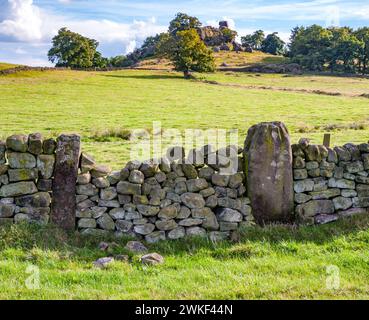 Eine Trockenmauer mit Blick auf den Robin Hoods Stride mit einem alten Torpfosten, der als Stein aus dem nahe gelegenen Nine Stones Close Stone Circle Derbyshire gedacht ist Stockfoto