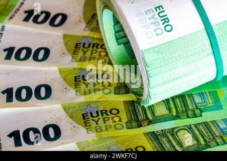 Eine Rolle von hundert Euro-Banknoten mit einem grünen Gummiband auf einem Hintergrund von 100 Euro-Banknoten, europäische Währung, Geld zu einer Rolle verdreht Stockfoto