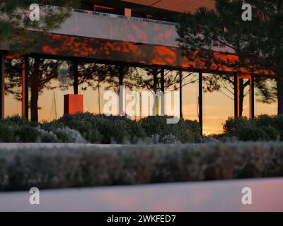 Fassade eines Gebäudes in den Sonnenstrahlen bei Sonnenuntergang. Reflexion des Sonnenuntergangs in den großen Glasfenstern eines Luxushotels. Landschaftsdesign. Ro Stockfoto