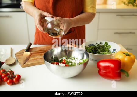 Weibliche Chefin in einer Uniform gießt Olivenöl aus einer Flasche. Kaukasische Bloggerin, die erklärt, wie man ein Gericht kocht Stockfoto