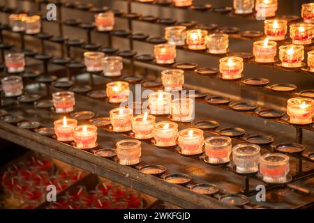 Viele brennende Opferkerzen oder Andachtskerzen in einer Kirche in kleinen Gläsern. Die Kerzen werden auf einen speziellen Kerzenständer gestellt, und die meisten davon sind ein Stockfoto