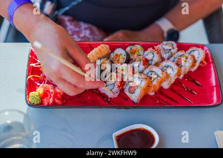 Nahaufnahme von weiblichen Händen, die Sushi mit Stäbchen vom Teller nehmen. Curacao. Stockfoto