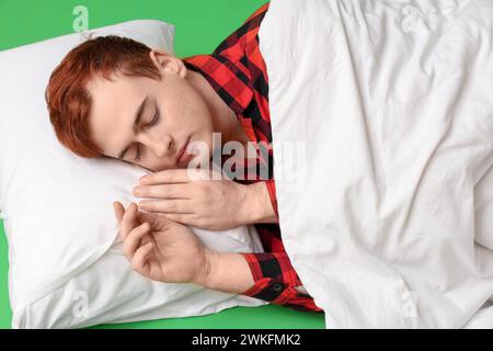 Hübscher junger Mann mit Decke und Kissen, der auf grünem Hintergrund schläft Stockfoto