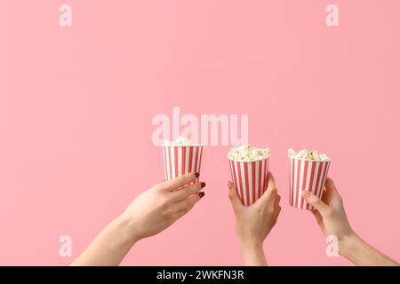 Hände halten Eimer mit Popcorn auf rosa Hintergrund Stockfoto