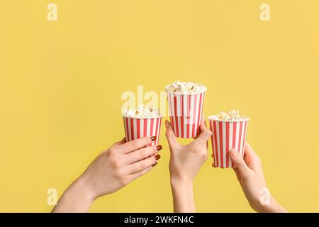 Hände halten Eimer mit Popcorn auf gelbem Hintergrund Stockfoto