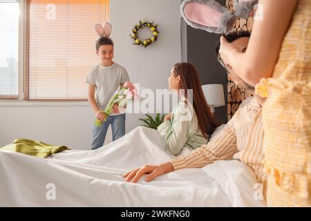 Der kleine Junge gibt seiner Mutter Tulpen im Schlafzimmer am Ostertag Stockfoto