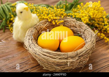 Süße Küken, Nest mit bemalten Ostereiern und Mimosa-Blumen auf hölzernem Hintergrund Stockfoto