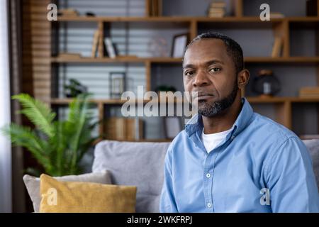 Porträt eines nachdenklichen Afroamerikaners mittleren Alters, der zu Hause auf einer Couch sitzt, reflektierend und gelassen wirkt. Stockfoto