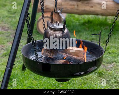 Kaffeekanne hängt über offenem Feuer und brennenden Baumstämmen. Stockfoto