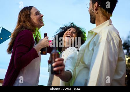 Konzentrieren Sie sich auf die aufgeregte Afrikanerin, die eine Bierflasche mit lachenden Millennials-Freunden auf dem Dach hält Stockfoto