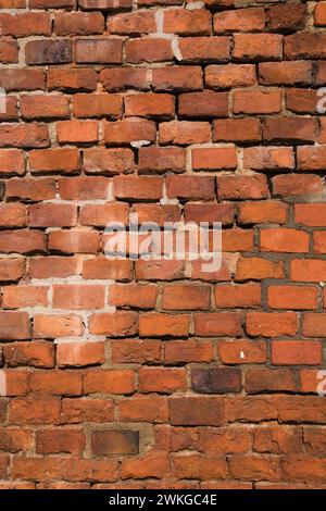 Nahaufnahme beschädigter rechteckiger roter Ziegelsteine und loser und fehlender Mörtelfugen an der Gebäudewand. Stockfoto