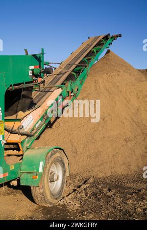 Grüner Stapelförderer und Hügel aus braunem Sand in kommerzieller Sandgrube. Stockfoto