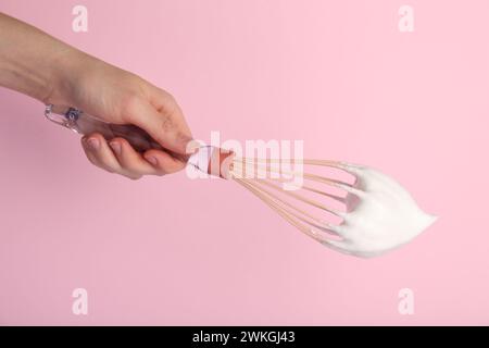 Frau mit Schneebesen mit Schlagsahne auf rosa Hintergrund, Nahaufnahme Stockfoto