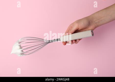 Frau mit Schneebesen mit Schlagsahne auf rosa Hintergrund, Nahaufnahme Stockfoto