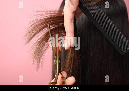 Friseur schneidet die Haare des Kunden mit einer Schere auf rosa Hintergrund, Großaufnahme Stockfoto