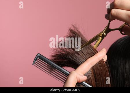 Friseur schneidet die Haare des Kunden mit einer Schere auf rosa Hintergrund, Großaufnahme Stockfoto