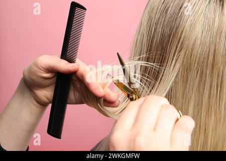 Friseur schneidet die Haare des Kunden mit einer Schere auf rosa Hintergrund, Großaufnahme Stockfoto