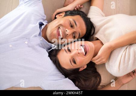 Blick von oben, Paare und lachen auf dem Boden im Wohnzimmer, entspannen und verbinden sich in einer romantischen Beziehung. Oben, Mann und Frau, die auf dem Boden liegen Stockfoto