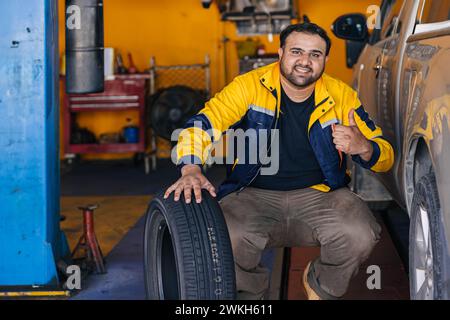 Porträt indischer Mann Arbeiter in der Garage Automechaniker glückliche Arbeit Autoservice ersetzen Reifenfahrzeug Wartung Stockfoto