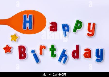 Happy Birthday geschrieben mit bunten Zuckerbuchstaben und einem orangen Löffel Stockfoto