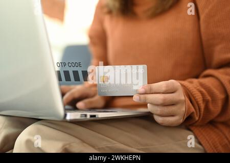 Junge Frau mit Kreditkarte und Eingabe des Verifizierungscodes Login zum Bankkonto auf Laptop Stockfoto
