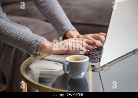 Weibliche Hände tippen auf einer Laptop-Tastatur auf dem Couchtisch im Wohnzimmer Stockfoto