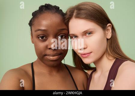 Close-up-Studio-Porträt von jungen Schwarzen und Kaukasierinnen ohne Make-up mit Sport-BHs, die in die Kamera schauen Stockfoto