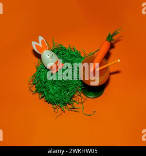 Osterei in einem Nest aus Gras und Karottensaft auf orangenem Hintergrund. Osterkonzept. Stockfoto
