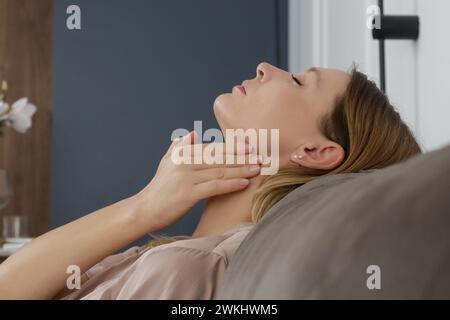 Eine kaukasische Frau, die ihren Hals berührt. Halsschmerzen, Erkältung, Grippe, Tonsillitis oder Schilddrüsenproblem Stockfoto