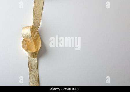 Glänzendes goldenes Textilband mit Knoten auf der linken Seite und isoliert auf weißem Hintergrund. Draufsicht. Stockfoto