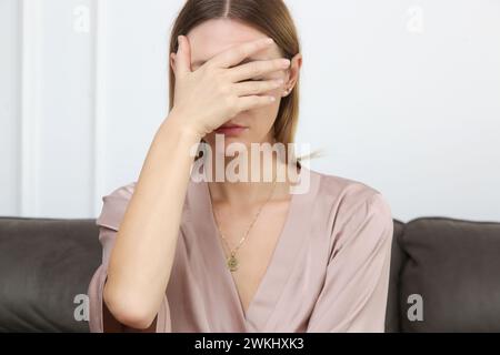 Das Porträt einer jungen depressiven Frau, die ihr Gesicht trauert, senkte ihren Kopf nach unten und saß auf dem Sofa. Vorstellung von schlechten Nachrichten, Scheidung, Trennung, Erschöpfung Stockfoto