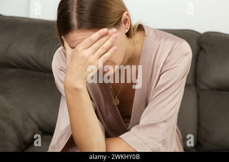 Das Porträt einer jungen depressiven Frau, die ihr Gesicht trauert, senkte ihren Kopf nach unten und saß auf dem Sofa. Vorstellung von schlechten Nachrichten, Scheidung, Trennung, Erschöpfung Stockfoto