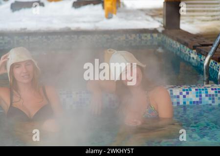 Zwei Frauen tragen Badeschutzhüte und entspannen sich in einem Whirlpool am Pool, genießen Freizeit und Spaß Stockfoto