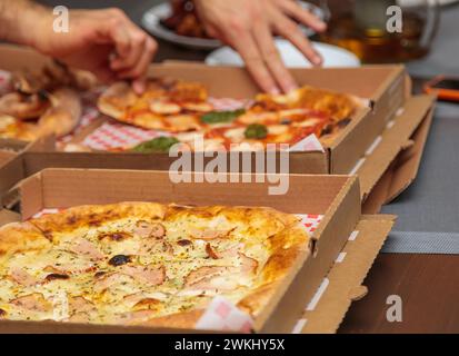 Mehrere Pizzen in Pappschachteln liegen auf einem Tisch ab und bieten eine Vielzahl von käsigen Belägen und herzhaften Zutaten. Ein Grundnahrungsmittel in der Küche, diese Di Stockfoto