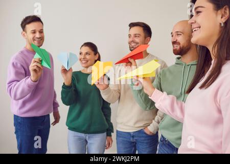 Gruppe glücklicher, lächelnder junger Leute, die bunte Origami-Flugzeuge zusammen fliegen Stockfoto