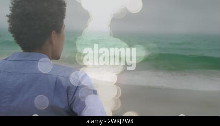 Bild von Lichtflecken über behindertem afroamerikanischen Mann, der im Rollstuhl sitzt Stockfoto